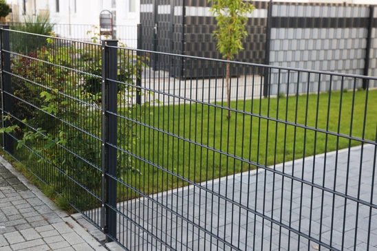 Scène extérieure résidentielle avec clôture métallique noire délimitant un espace vert